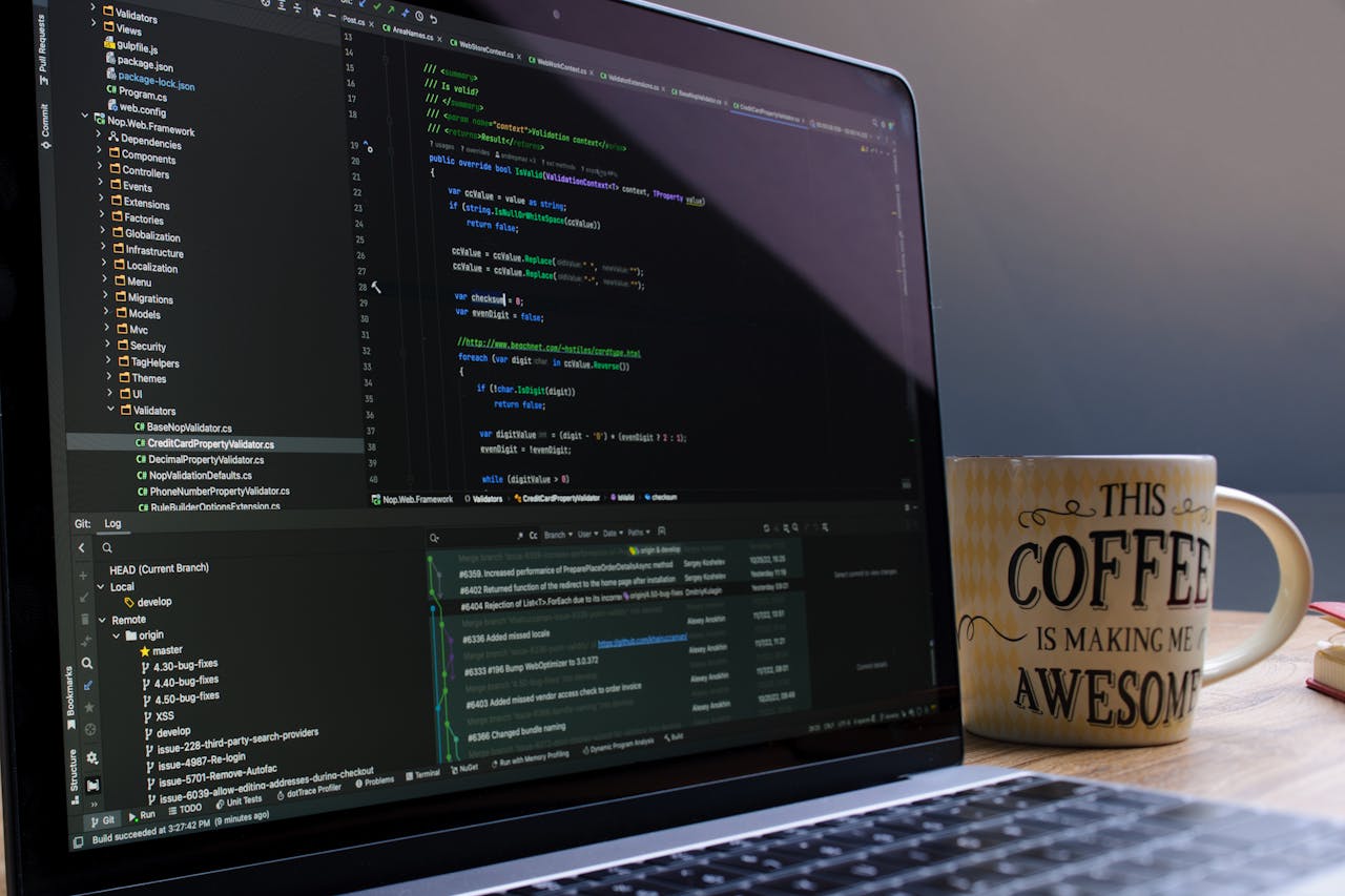 Close-up of laptop with coding software and a motivational coffee mug on a desk.